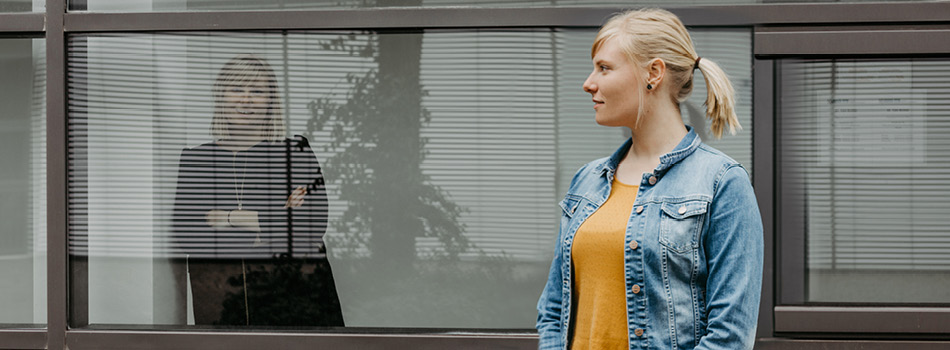 Bild zweier Frauen, eine steht hinter dem Bürofenster, eine läuft vorbei. 
